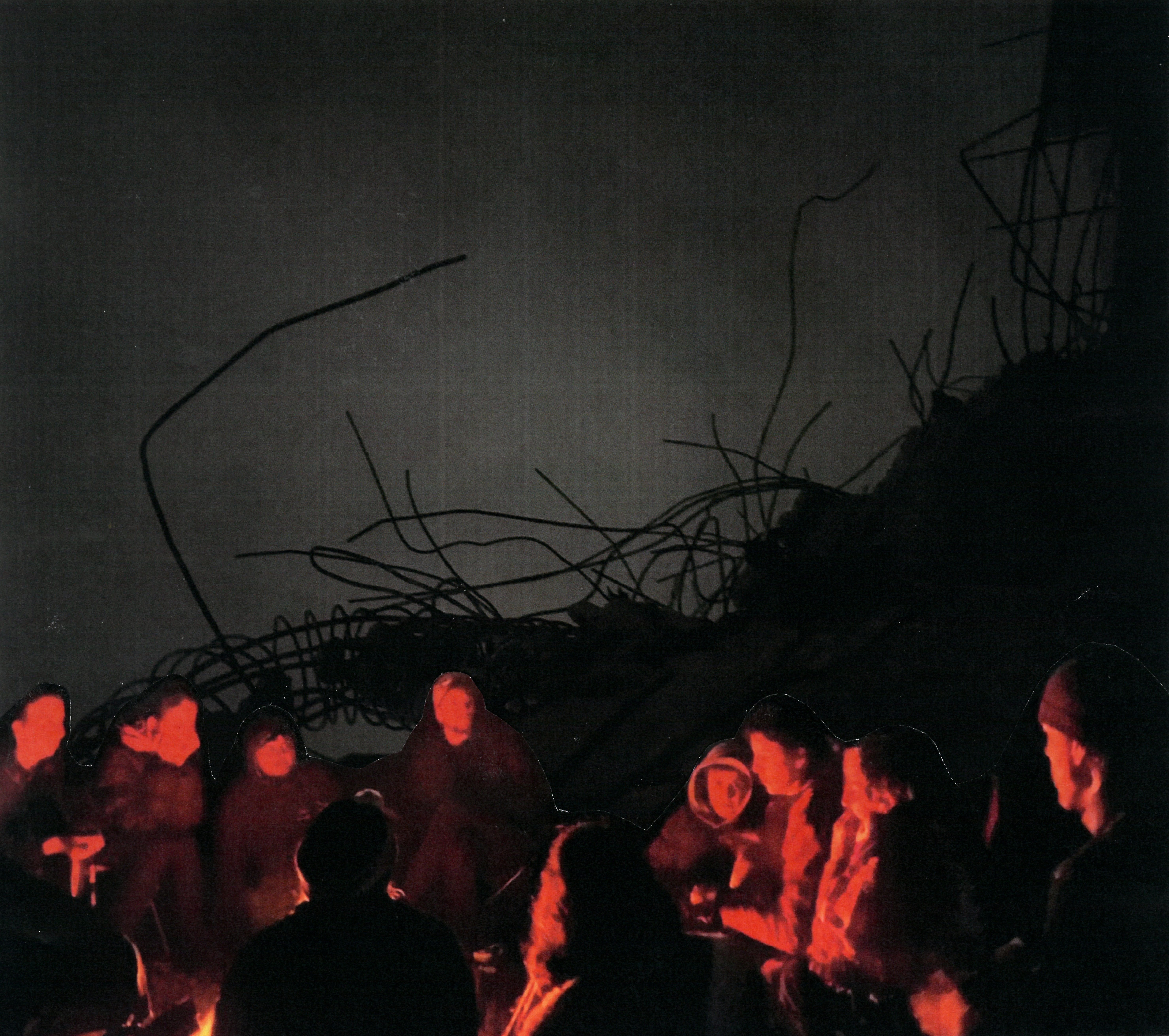 A group gathers around a fire. Behind them, a dark tangle of twisted rebar.